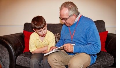 Volunteer reading with a child both sitting on a sofa