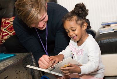 Volunteer and child reading a book and laughing