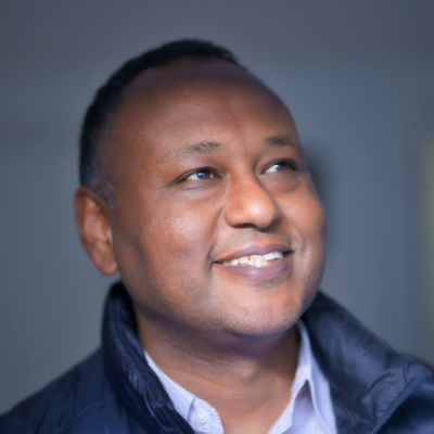 A smiling man looking upwards, away from the camera, in front of a blank wall