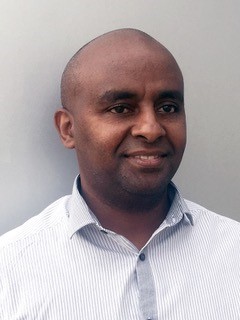 a smiling man in a white shirt, in front of a blank wall